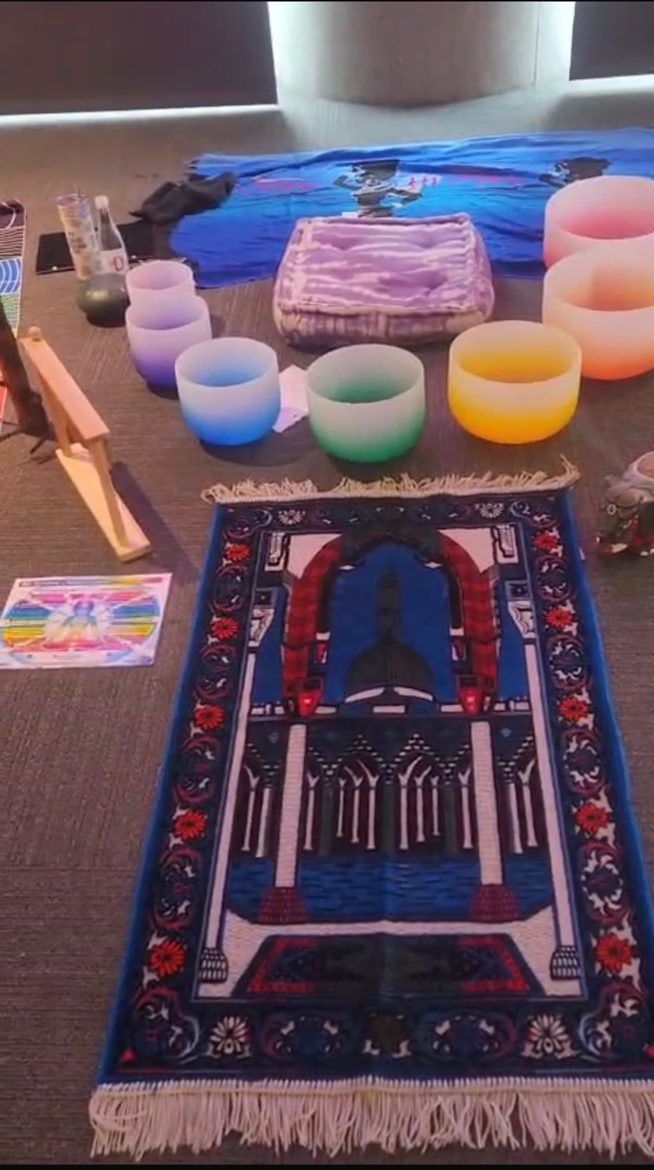 Crystal singing bowls, a prayer rug, and a chakra chart laid out on the floor before a session